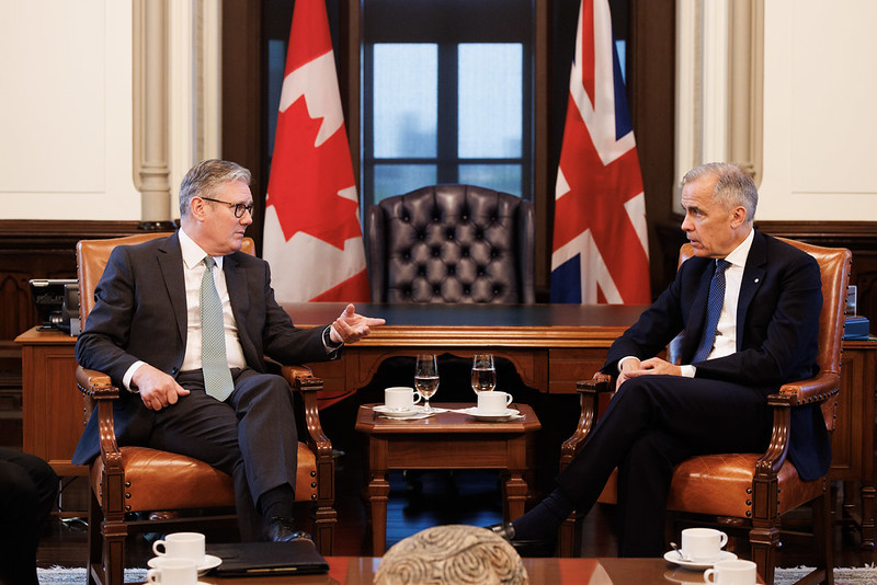 Keir Starmer and Mark Carney sit in front of a desk and a Canadian and UK flag