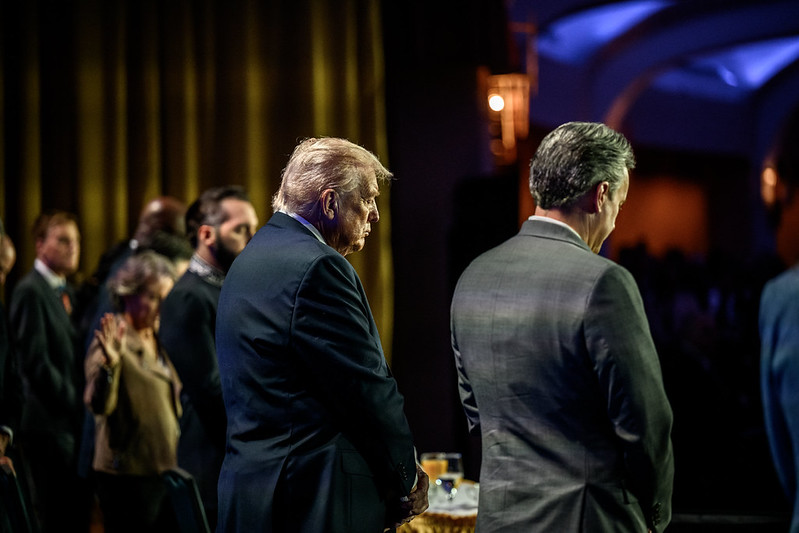 Donald Trump is visible from the side as he bows in prayer next to a man in a grey suit