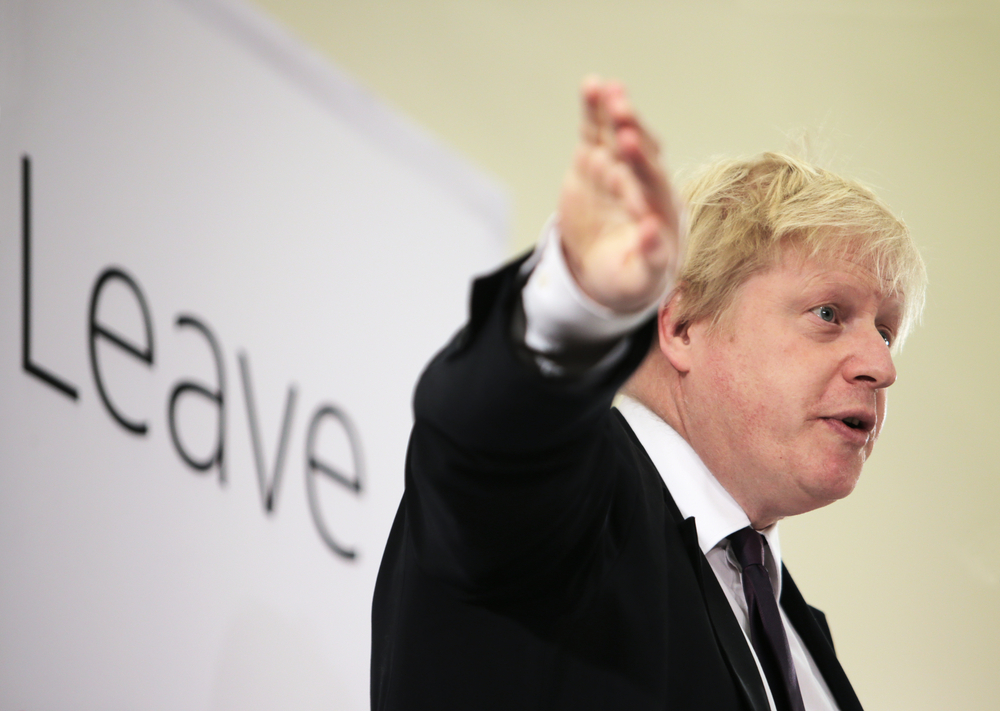 Boris Johnson stands with an arm raised in front of a Leave banner.