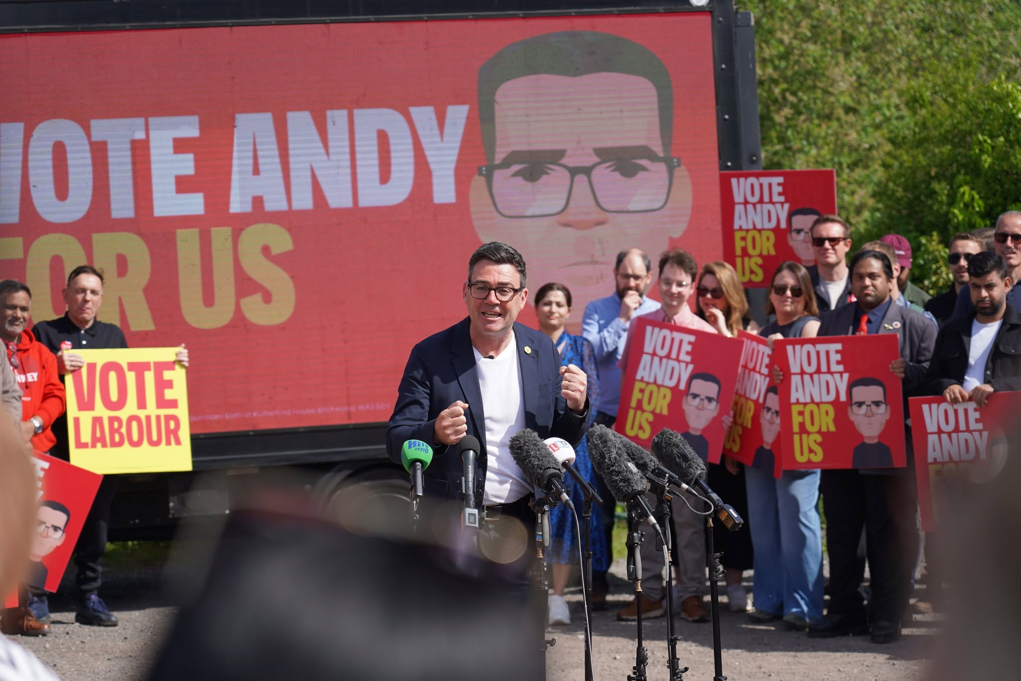 Andy Burnham stands in front of microphones and supporters